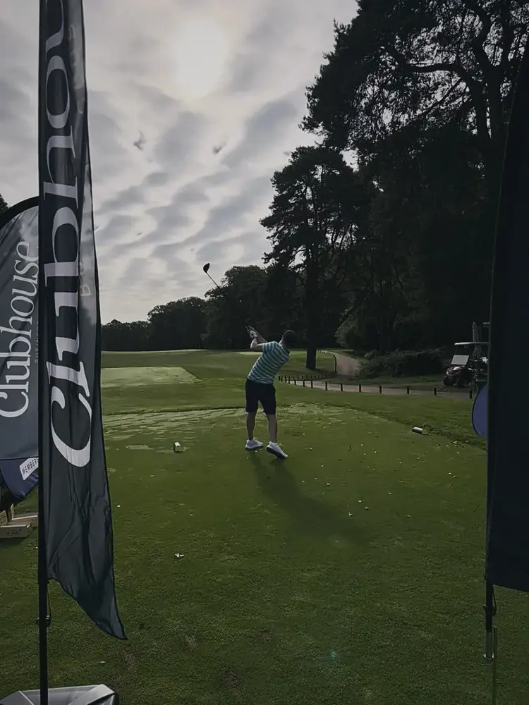 A player driving off the first tee at Woburn, with Clubhouse flags beside the tee