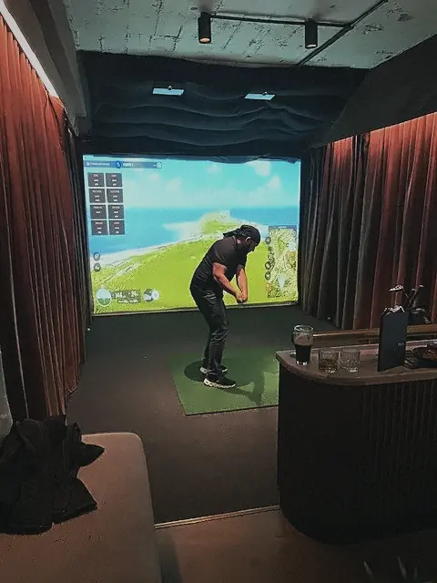 A guest taking a swing on a golf simulator at a Clubhouse evening at Pitch