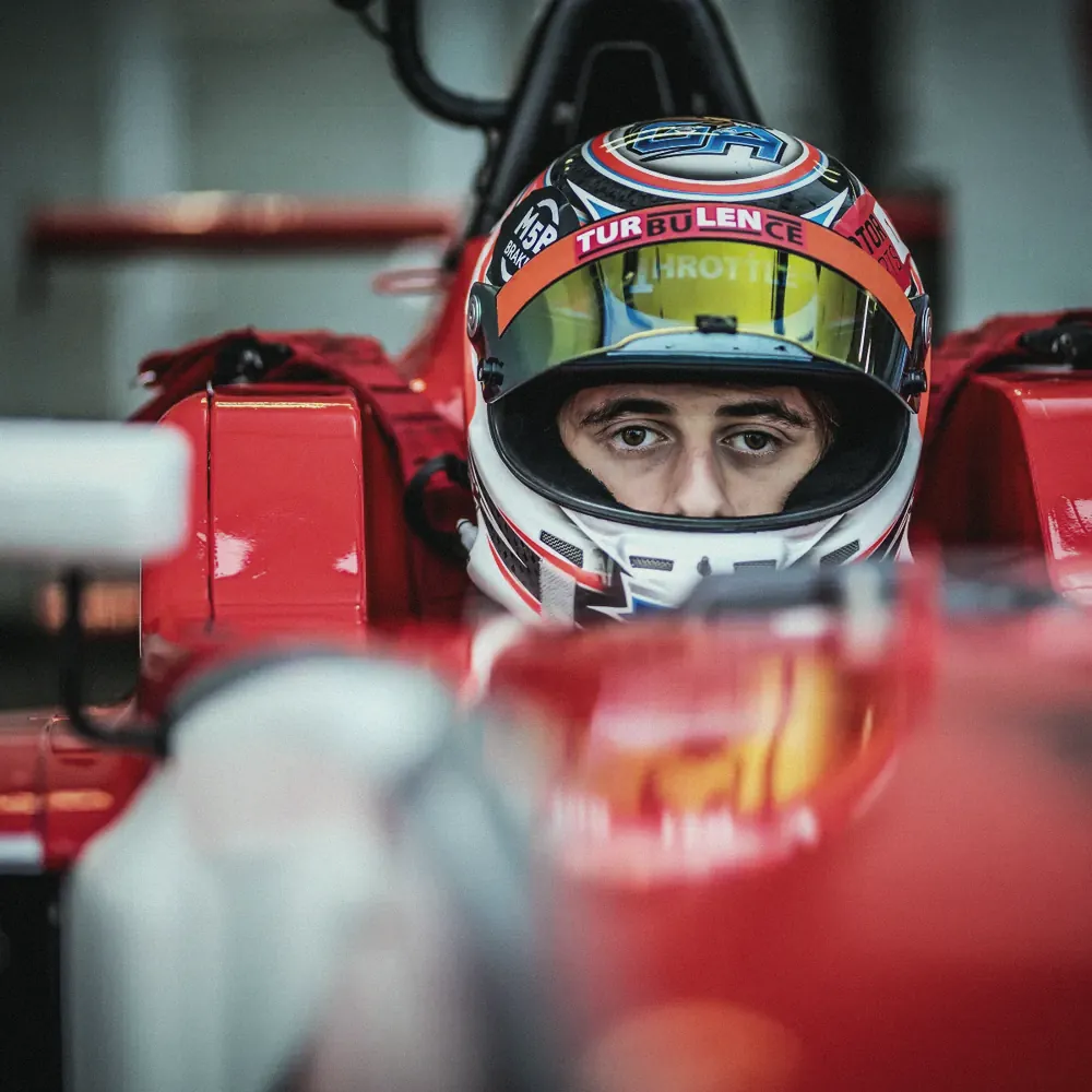Formula 1 driver in a helmet sitting in a red car